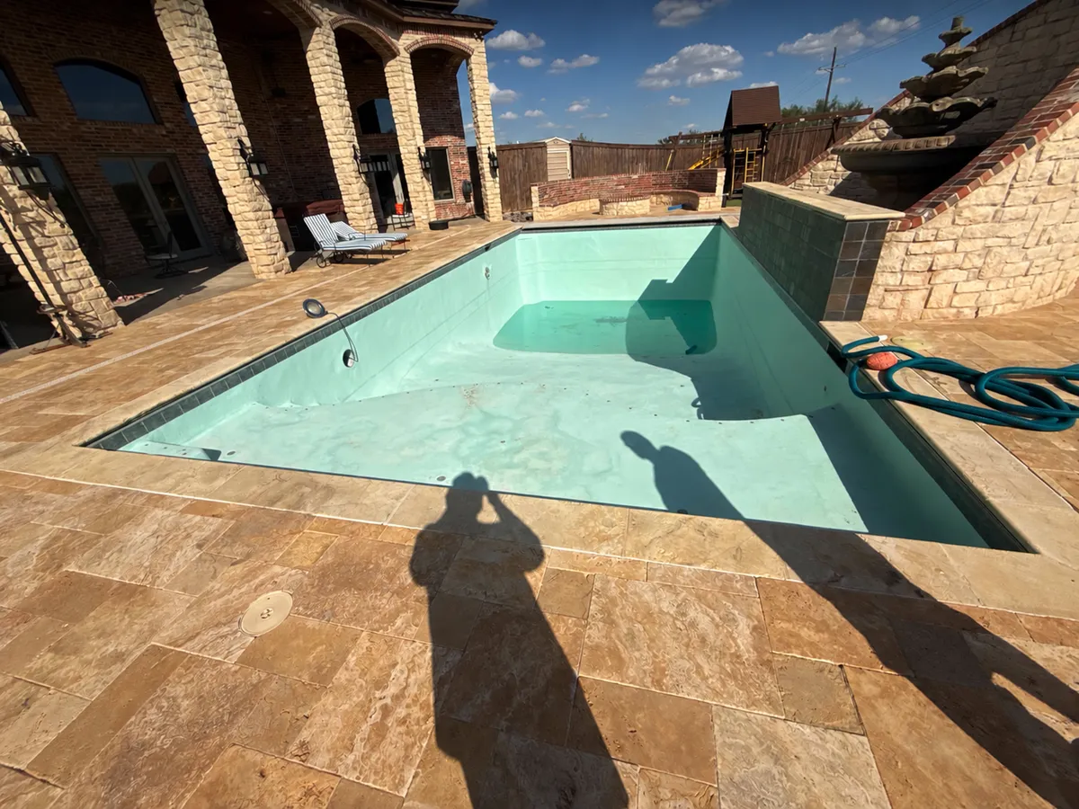 Before: Drained pool with a light finish and dolphin designs beside a stone patio